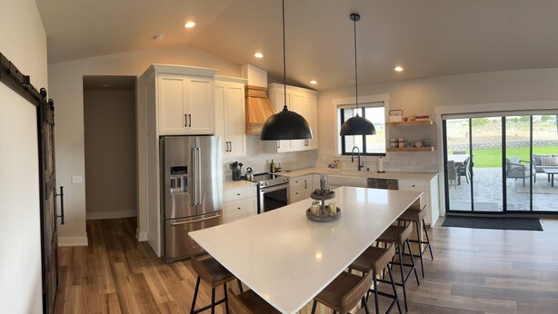 A modern kitchen with white cabinets, stainless steel appliances, and a large island with bar stools. - New Custom Multi Master + Sleeping Room Golf Course Home w/ Outdoor Living Area  (Mattawa)