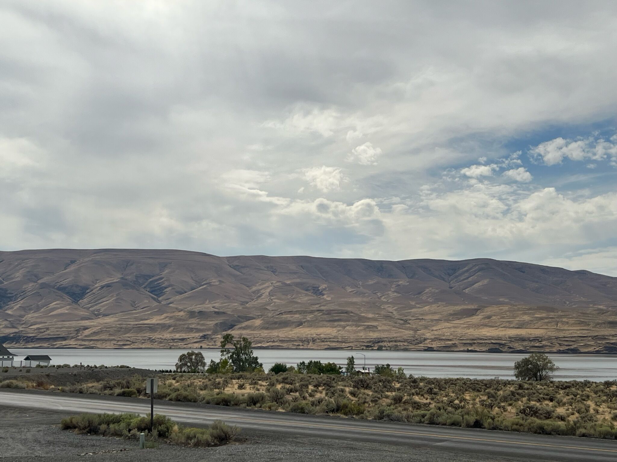 A road with a view of a lake and mountains in the distance.