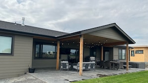 A modern house with a covered patio area featuring outdoor furniture and a grill. - New Custom Multi Master + Sleeping Room Golf Course Home w/ Outdoor Living Area  (Mattawa)