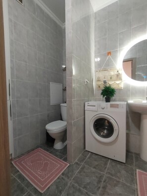 A compact bathroom with a toilet, washing machine, and sink.