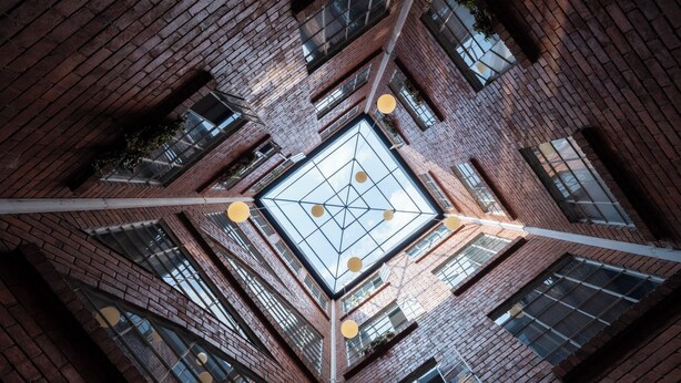 A high-angle view of a building with a central glass atrium, brick walls, and multiple windows. - 5Q House Quinta Camacho (Bogotá)