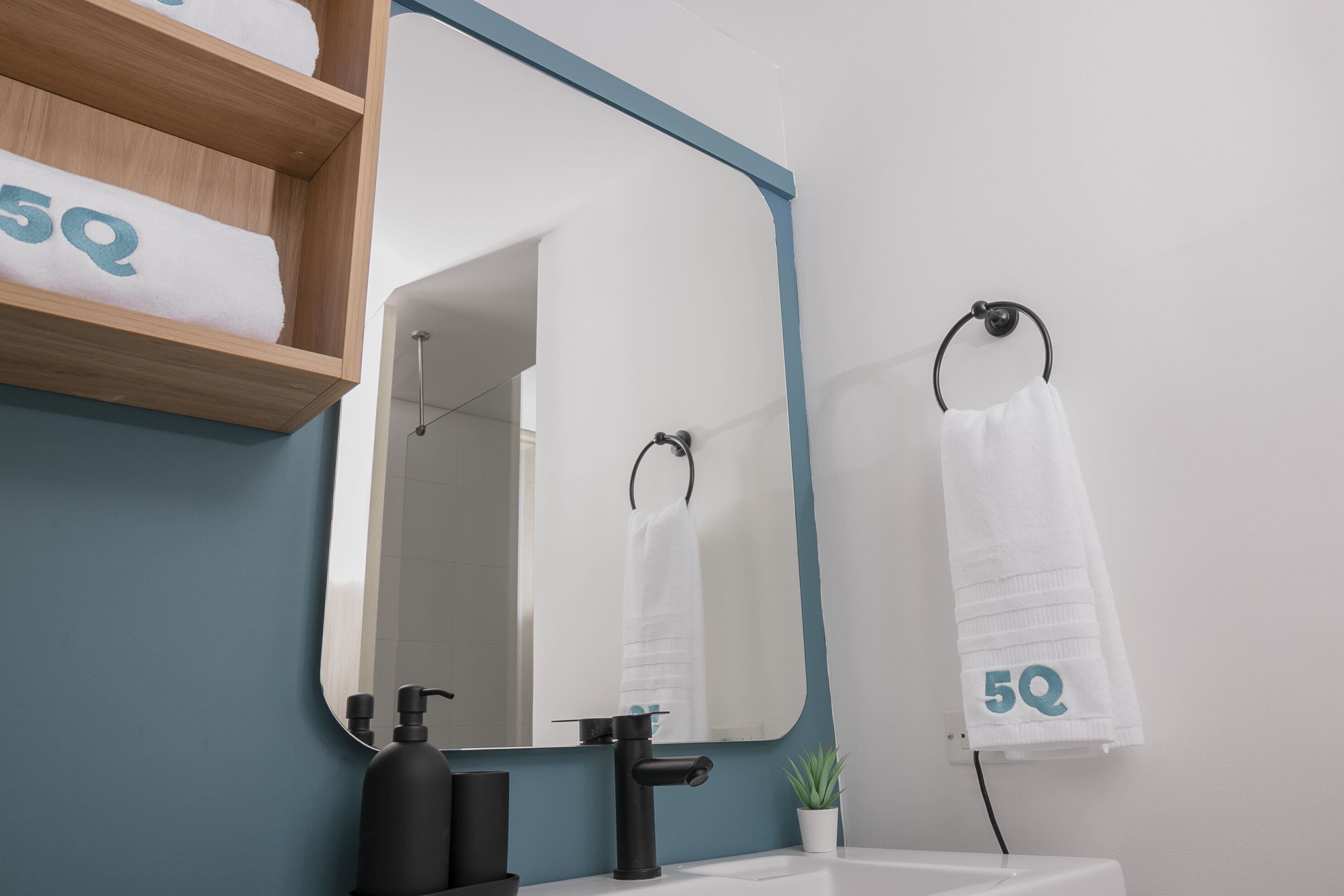 A bathroom with a wooden shelf holding towels, a mirror, a sink, and a potted plant.