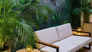 A modern interior with a sofa, a round wooden table with a lamp, and a mural of a monkey on a vine. - 5Q House Quinta Camacho (Bogotá)