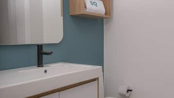 Une salle de bain avec un lavabo blanc, un miroir, des toilettes et une étagère avec des serviettes.