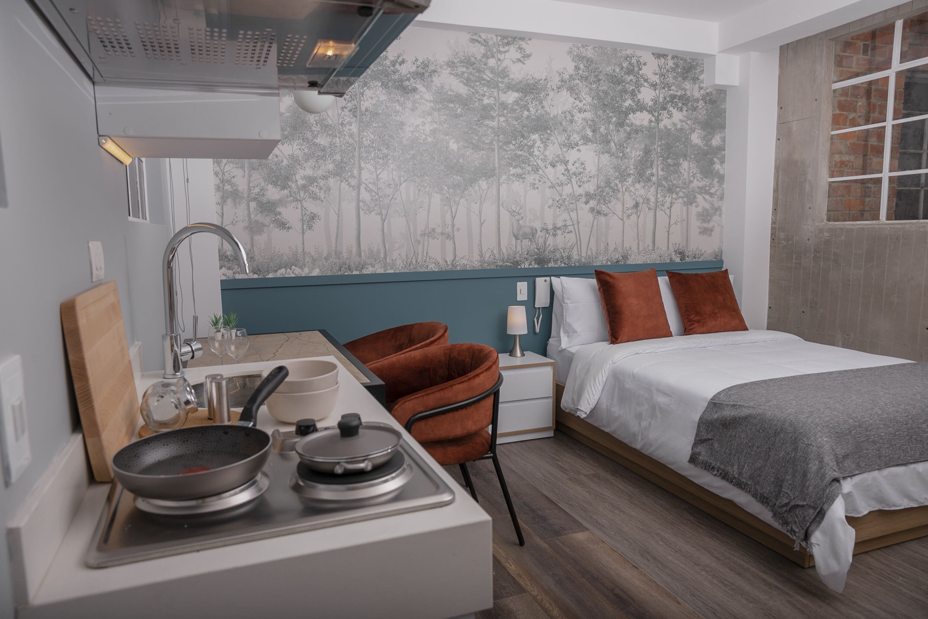 Una habitación moderna con cama, una kitchenette pequeña y un mural en la pared.
