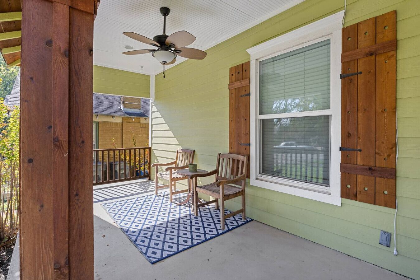 A covered porch with a ceiling fan, two wooden chairs, and a patterned rug.