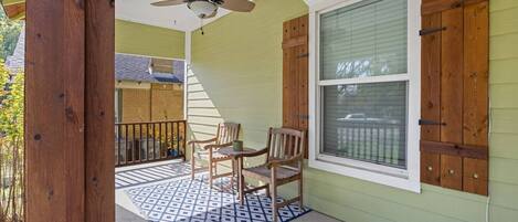 A covered porch with a ceiling fan, two wooden chairs, and a patterned rug.