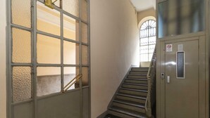 Una scala con pavimento a scacchi, una porta metallica con vetri e una ringhiera in metallo.