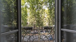 Vista attraverso una finestra con ringhiera di un balcone in metallo, alberi e auto parcheggiate.