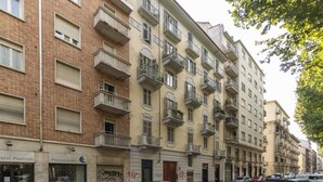 Un edificio residenziale a più piani con balconi, auto parcheggiate e vetrine.
