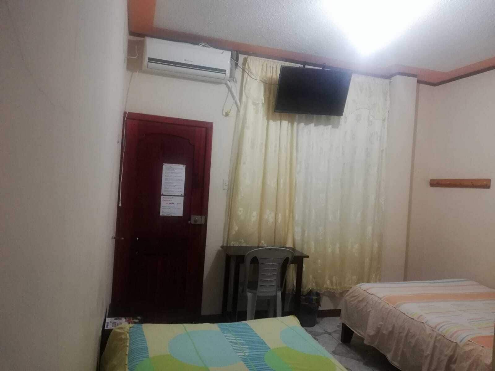 Una habitación pequeña y sencilla con una cama, un escritorio y un televisor montado en la pared.