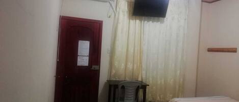 Una habitación pequeña y sencilla con una cama, un escritorio y un televisor montado en la pared.