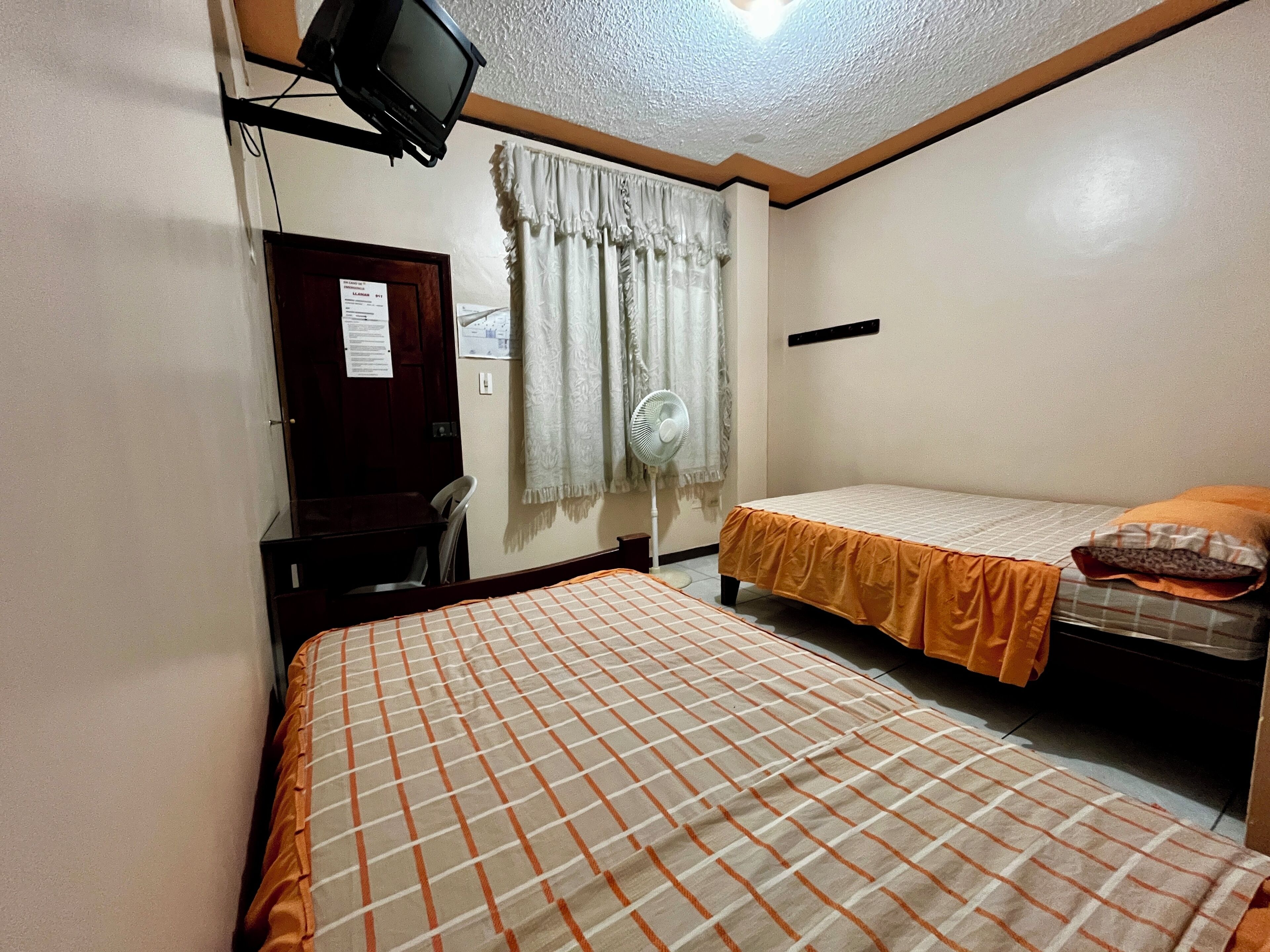 Una habitación con dos camas, un escritorio, una silla, un televisor y un ventilador.
