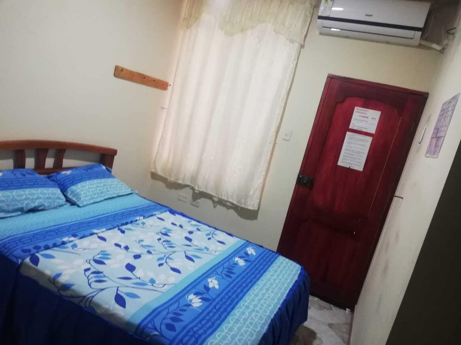 Un dormitorio con una cama, una puerta roja y un equipo de aire acondicionado.