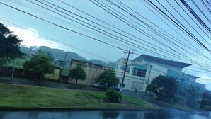 A residential area with a two-story building, a grassy area, and parked cars. - Hostal Amazónico Bello Amanecer (Nueva Loja)