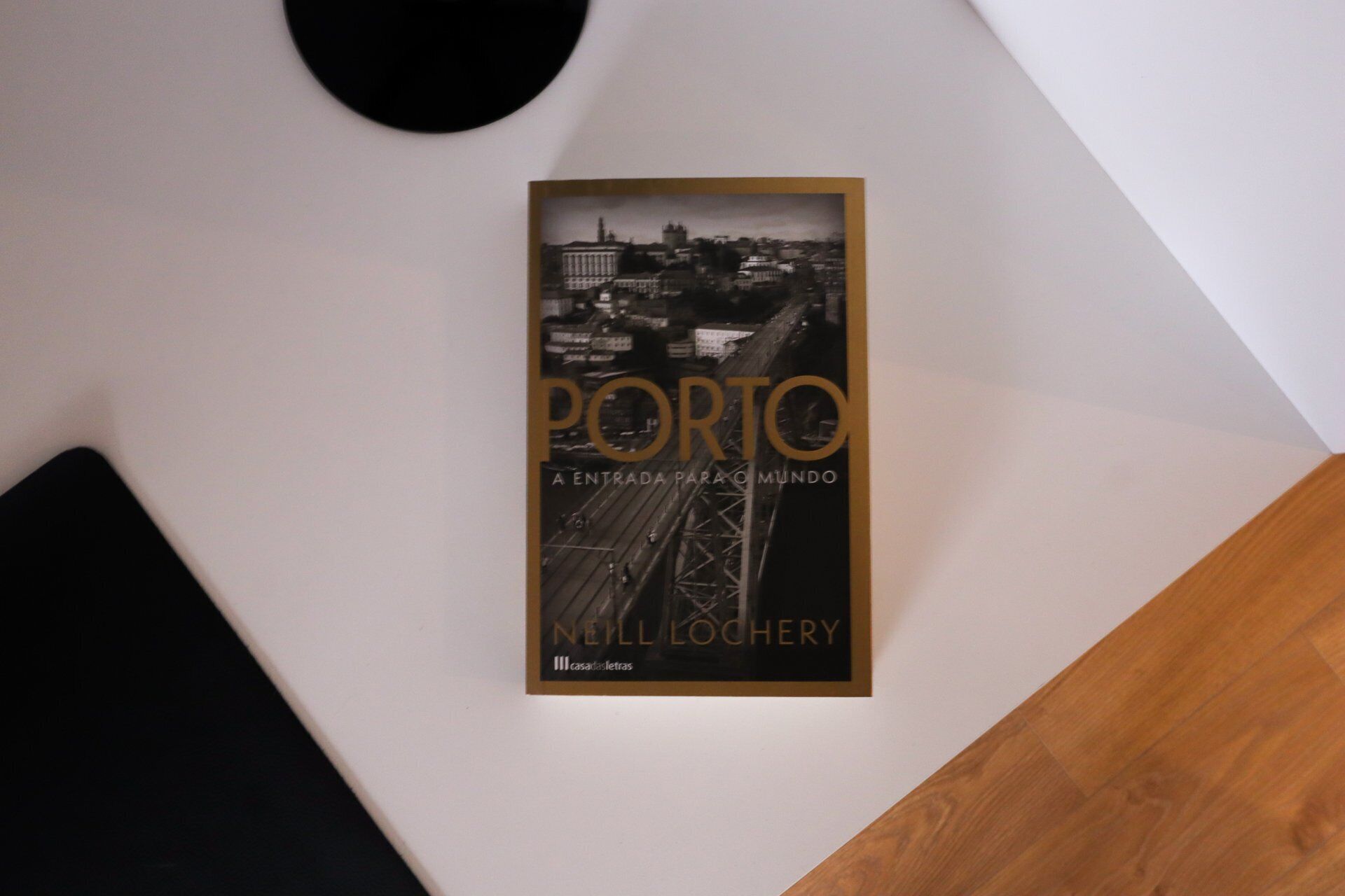 Un llibre amb el títol 'PORTO A ENTRADA PARA O MUNDO' de Nell Lochery, col·locat sobre una paret blanca.