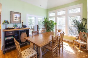 Una sala da pranzo con tavolo e sedie in legno, ampie finestre e diversi elementi decorativi.