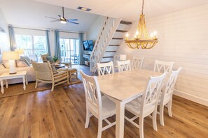 A spacious living room with a dining area, wooden flooring, white furniture, a chandelier, and a staircase leading to another level. - Palms North 3b - Sea La Vie - Deeded Beach Access! (Santa Rosa Beach)