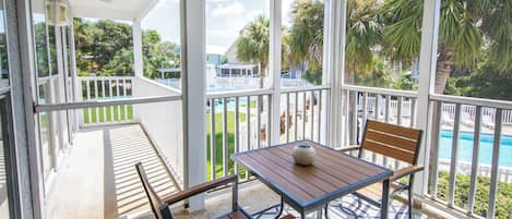 A covered outdoor area with a table and chairs, a view of a pool, and a white fence.