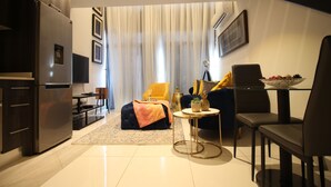 A modern living room with a sofa, coffee table, and a dining area with chairs. - Embassy Gardens - One Bed (Accra)