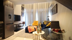 A modern living room with a sofa, chairs, a glass table, and a dining table. - Embassy Gardens - One Bed (Accra)