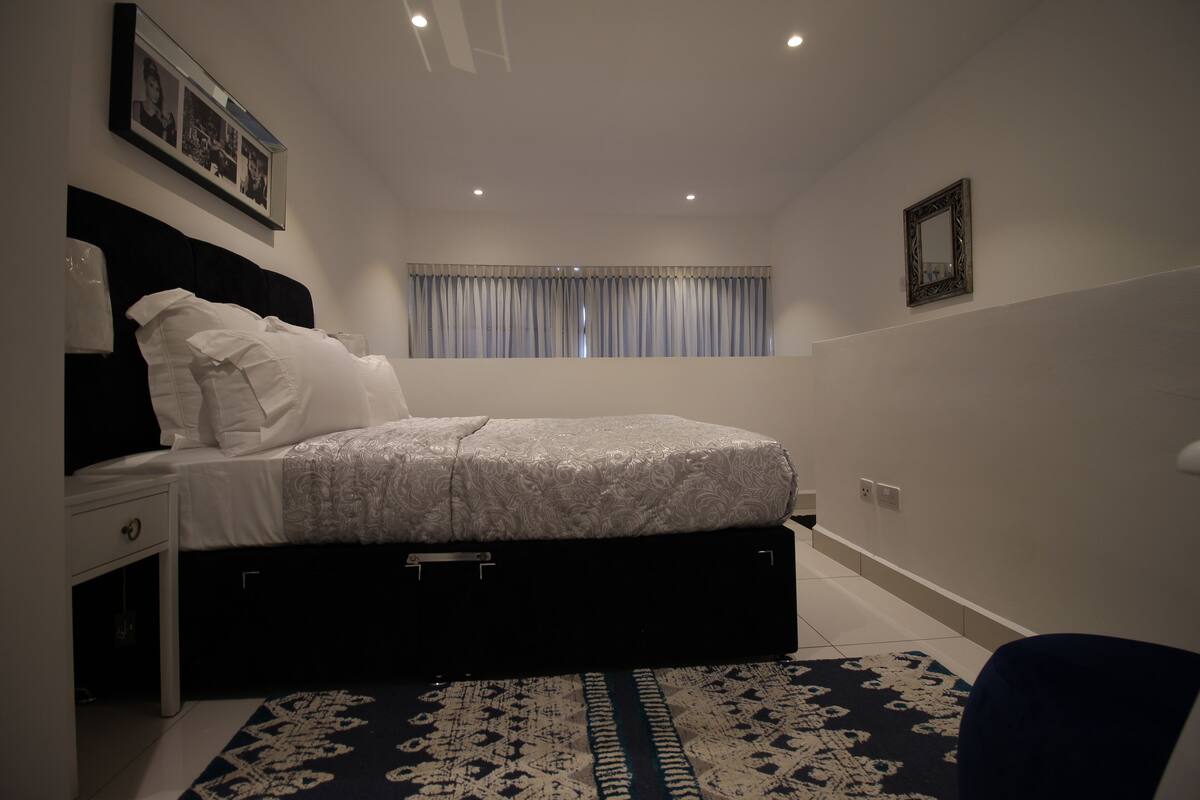 A bedroom with a bed, bedside table, and a window with curtains.