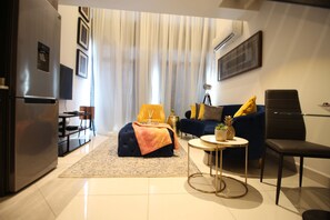 Un saló modern amb un sofà, un pouf i una taula de centre. Hi ha una zona de dinar amb taula i cadires.