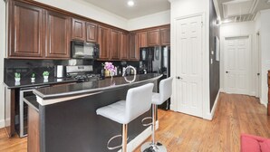 A modern kitchen with dark wooden cabinets, stainless steel appliances, and a black countertop. - Love&Mystique Getaway in Galleria w/ Pool //Sleeps12! (Houston)