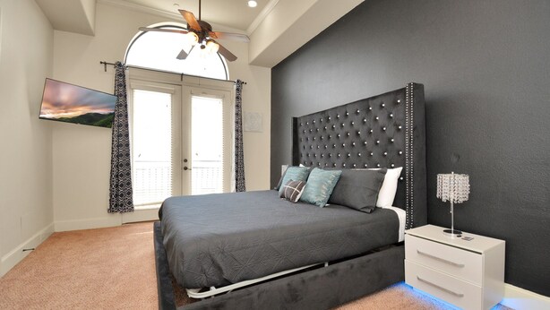 A bedroom with a bed, a nightstand, a ceiling fan, and a TV mounted on the wall. - Love&Mystique Getaway in Galleria w/ Pool //Sleeps12! (Houston)