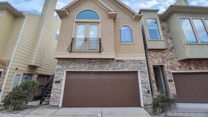 A two-story house with a stone facade, a brown garage door, and a small balcony. - Love&Mystique Getaway in Galleria w/ Pool //Sleeps12! (Houston)