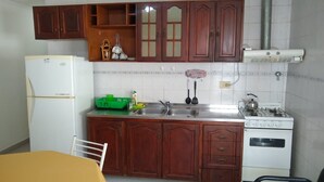 Une cuisine de taille réduite, avec des meubles en bois, un réfrigérateur blanc, une cuisinière à gaz et un évier.