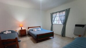 Une chambre d’hôtel avec trois lits, une table de chevet avec une lampe, une fenêtre avec des rideaux et un appareil de climatisation.