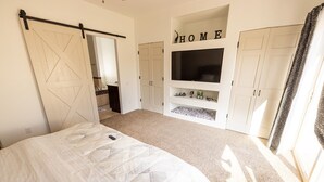 A bedroom with a bed, a sliding door, a TV, and a 'HOME' sign on the wall. - Desert Ranch House (Page)