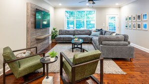 Una sala moderna con un sofá seccional, un sillón verde, una mesa de centro y un televisor de pantalla plana montado en una pared de madera decorativa.