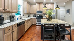 Una cocina moderna con armarios de madera, electrodomésticos de acero inoxidable y encimera de granito, con una isla central y taburetes de bar.