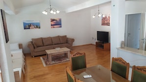 A living room with a sofa, a coffee table, a TV, and a dining area with chairs.