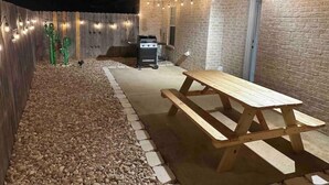 Eine Außenpatio mit Holztisch, Grill und Lichterkette.