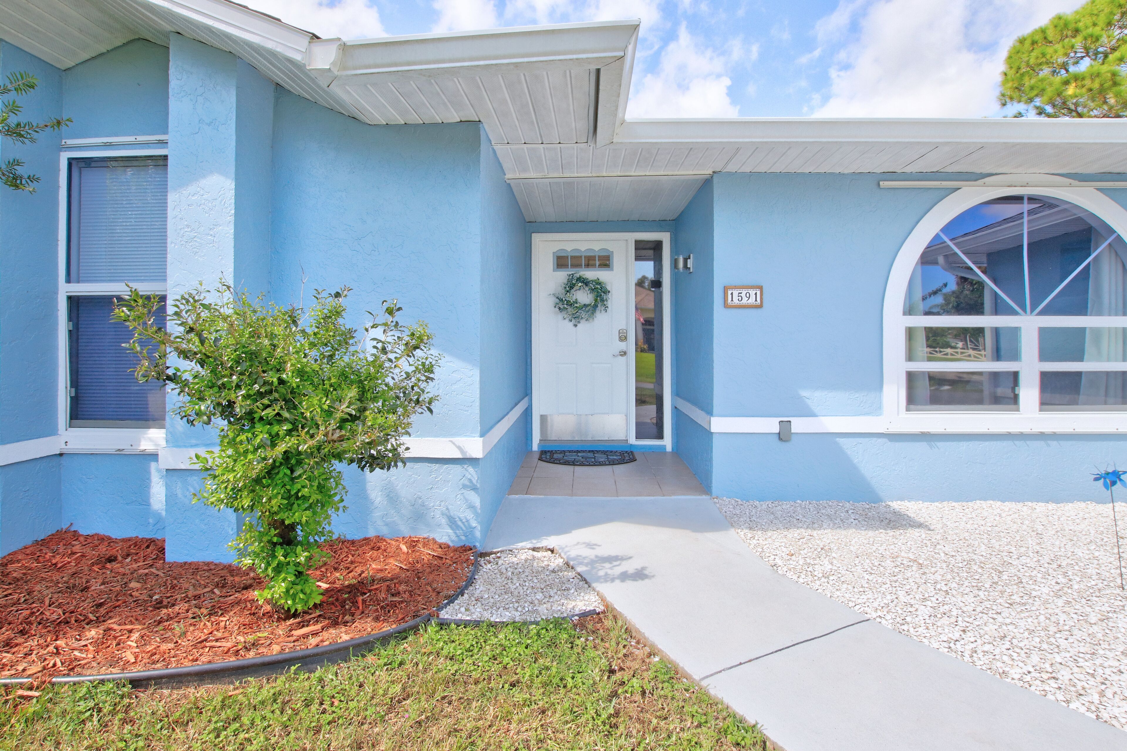 A house with a blue exterior, a front door with a wreath, and a mailbox.