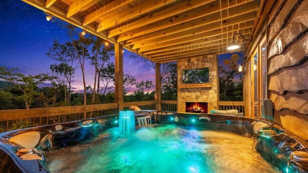 Un área de hidromasaje con chimenea de piedra, vigas de madera y un cielo estrellado.