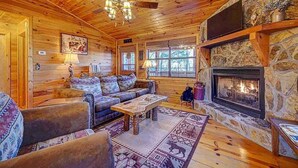 A cozy log cabin interior with a stone fireplace, wooden furniture, and a large window. - Amy's Blue Ridge Mtn & Starlight View (Ellijay)