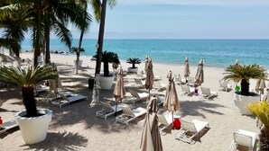 A beachside resort with sun loungers, umbrellas, and palm trees.