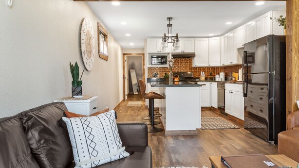 A modern kitchen with white cabinets, a central island, and a black refrigerator. - Stylish Uptown Butte Condo - 632 (Butte)