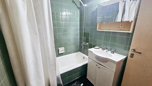 A bathroom with green tiles, a white bathtub, a sink, and a mirror. - 2 ambientes zona facultad de medicina (Buenos Aires)