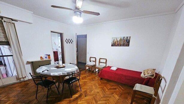 A room with a wooden herringbone floor, a round dining table with chairs, a red sofa, a ceiling fan, and a painting on the wall. - 2 ambientes zona facultad de medicina (Buenos Aires)