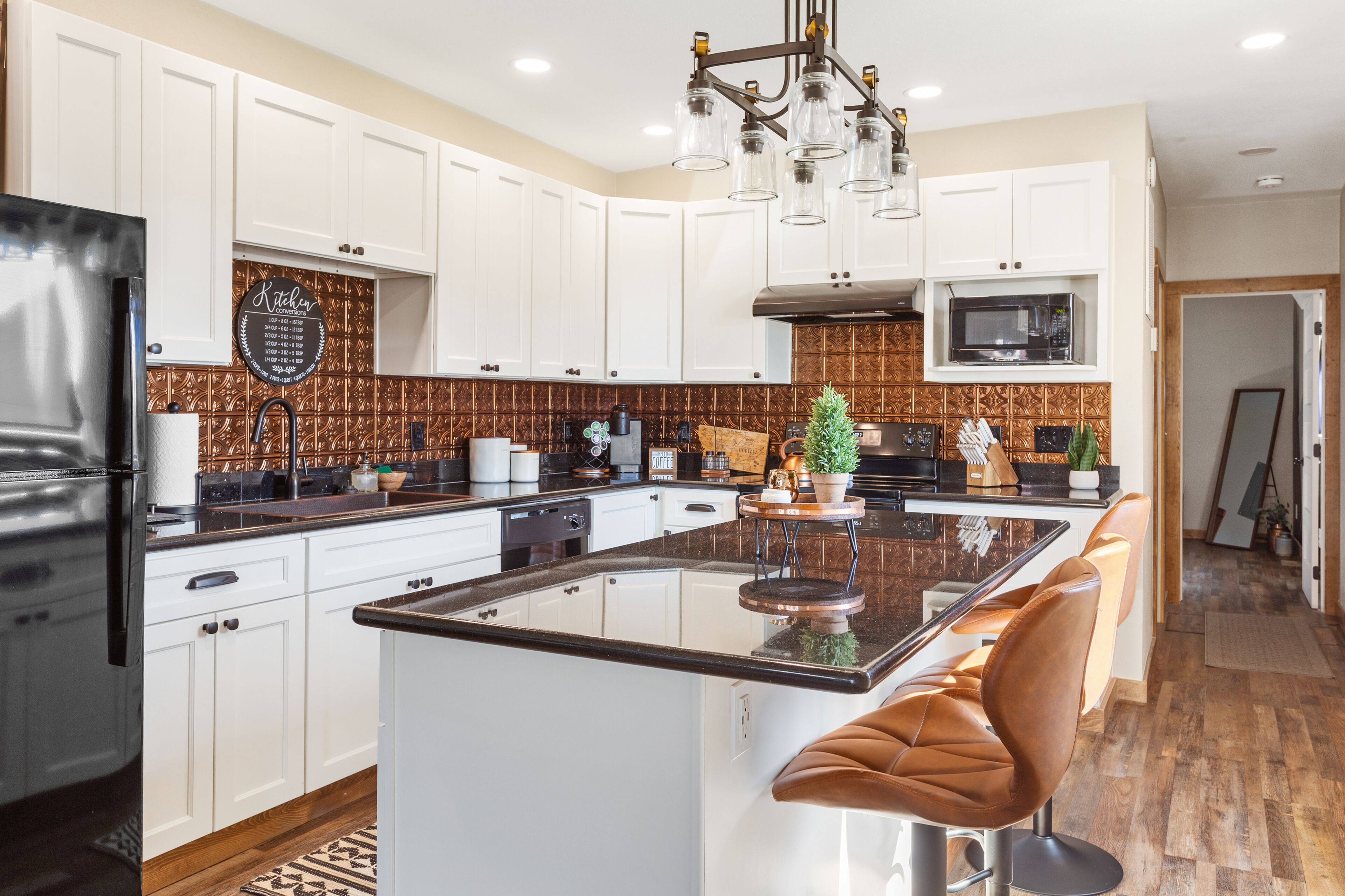 Una cocina moderna con armarios blancos, una isla central con taburetes, un refrigerador de acero inoxidable y un microondas.