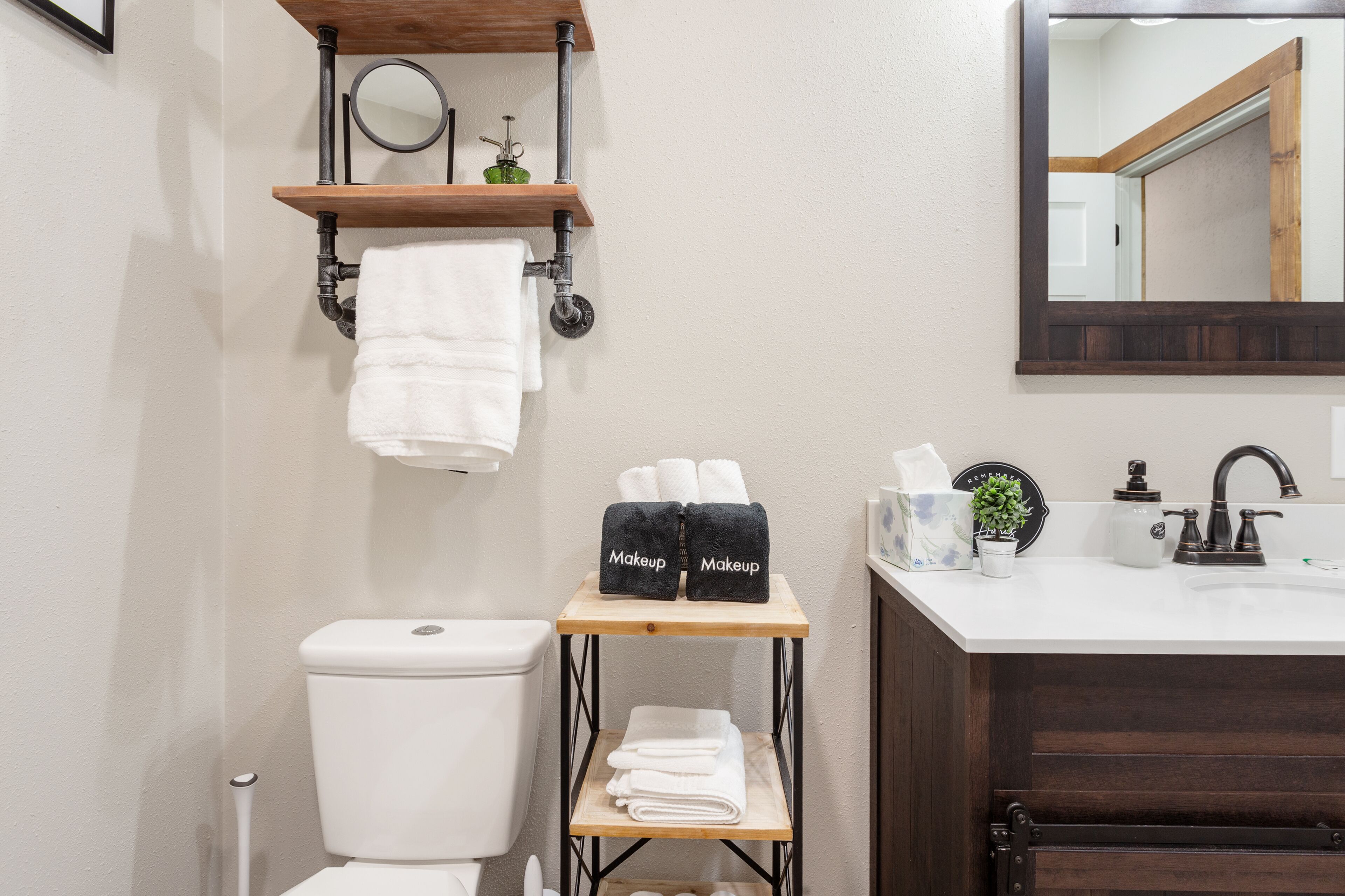 A bathroom with a toilet, sink, and mirror. There are towels and a shelf with toiletries.