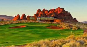 A modern building with a glass facade, situated on a golf course with red rock formations in the background.