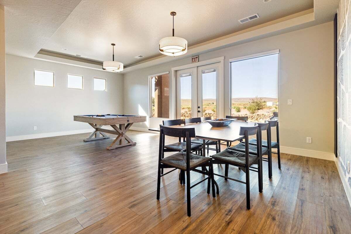 Een ruime kamer met een pooltafel, een eettafel met stoelen, en grote ramen met uitzicht op de woestijn.