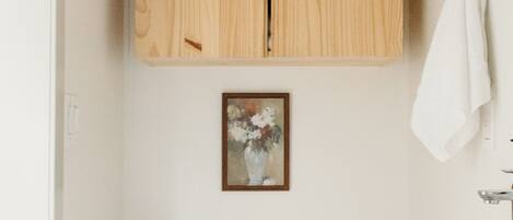 Un baño pequeño con un inodoro blanco, armarios de madera, un lavamanos y un cuadro en la pared.