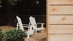 Zwei weiße Adirondack-Stühle in einer Gartenanlage mit Holzhäcksel und Grünpflanzen.